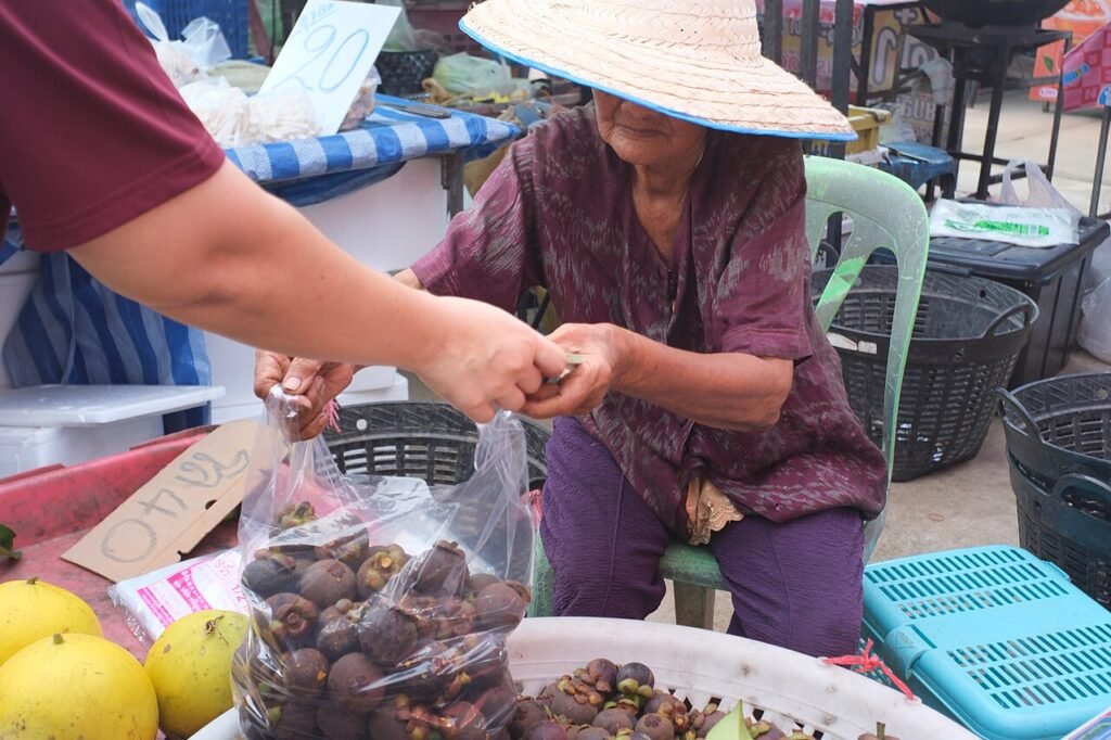 Idős árus mangosztánt ad át egy piacon Thaiföldön